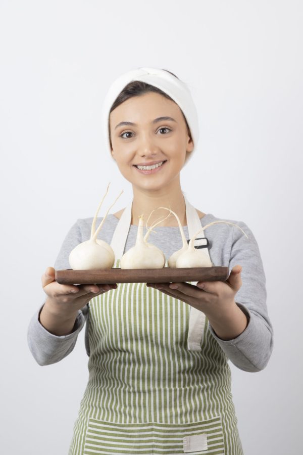 Portrait of a young girl model holding a wooden board with white radishes . High quality photo